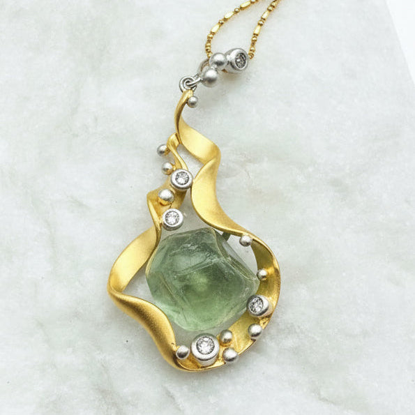 Gold necklace with a green stone pendant on a marble surface