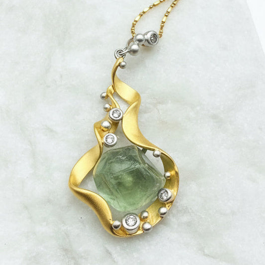 Gold necklace with a green stone pendant on a marble surface