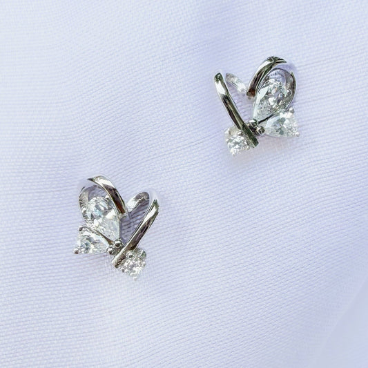 Butterfly-shaped earrings with clear gemstones on a light purple background