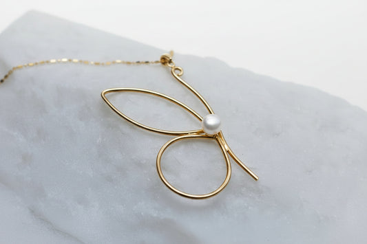 Gold necklace with a pearl pendant on a light gray surface