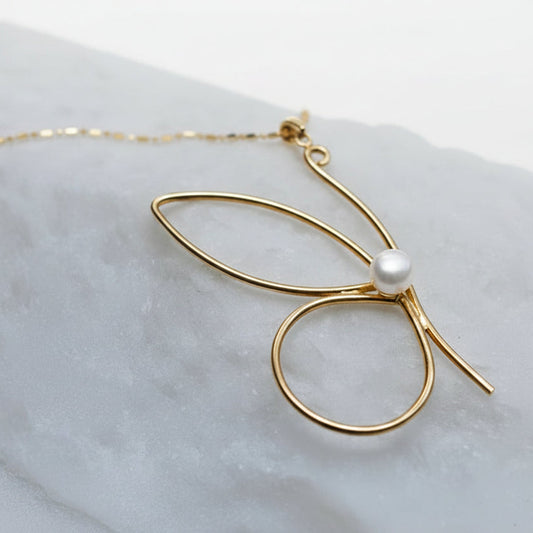 Gold necklace with a pearl pendant on a light gray surface