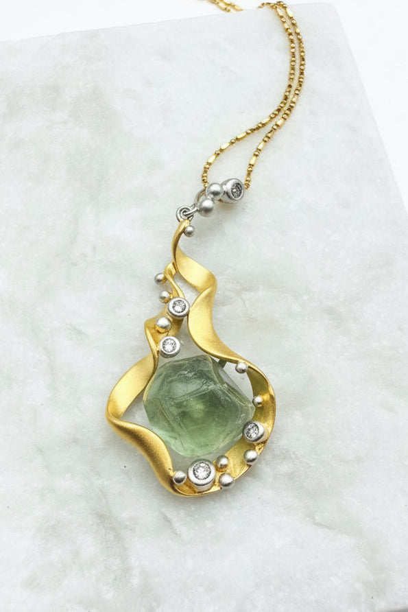 Gold necklace with a green stone pendant on a marble surface