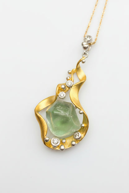 Gold pendant with green stone and small crystals on a white background