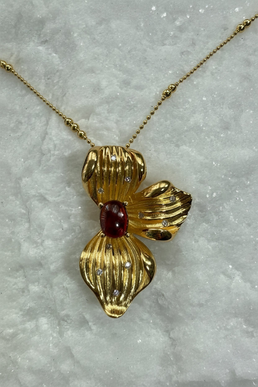 Gold pendant with a red gemstone on a marble surface
