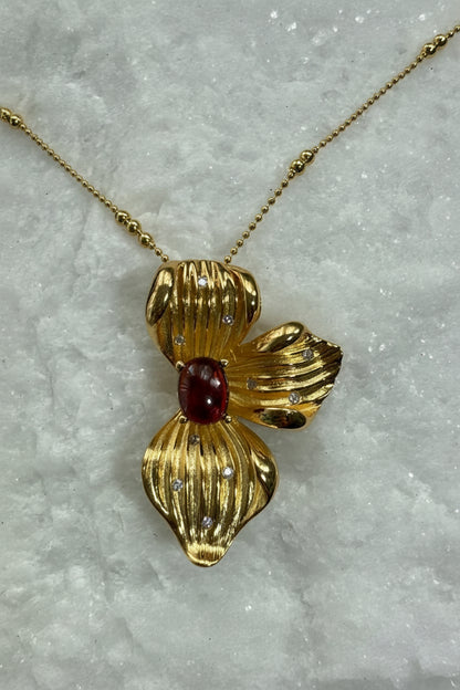 Gold pendant with a red gemstone on a marble surface
