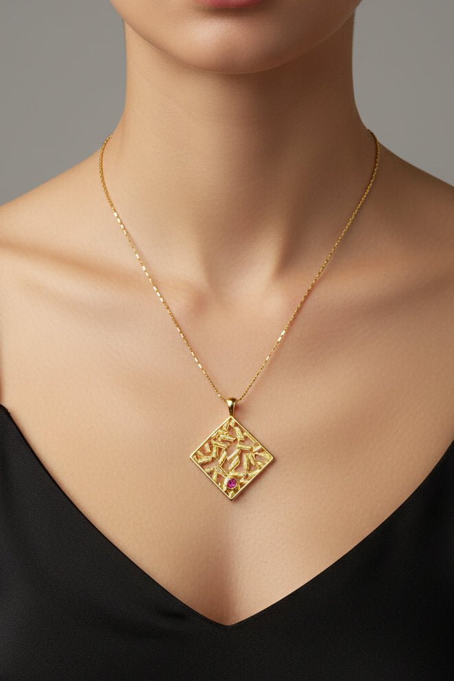 Gold necklace with a square pendant featuring a red gemstone on a light green cushion.