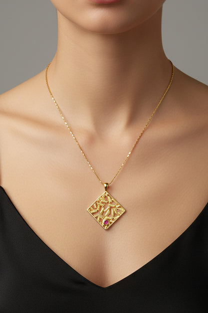 Gold necklace with a square pendant featuring a red gemstone on a light green cushion.