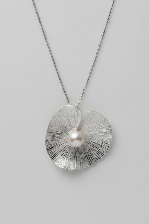 Silver necklace with a textured pendant and pearl on a gray surface