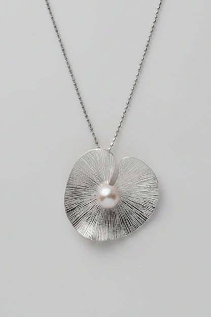 Silver necklace with a textured pendant and pearl on a gray surface