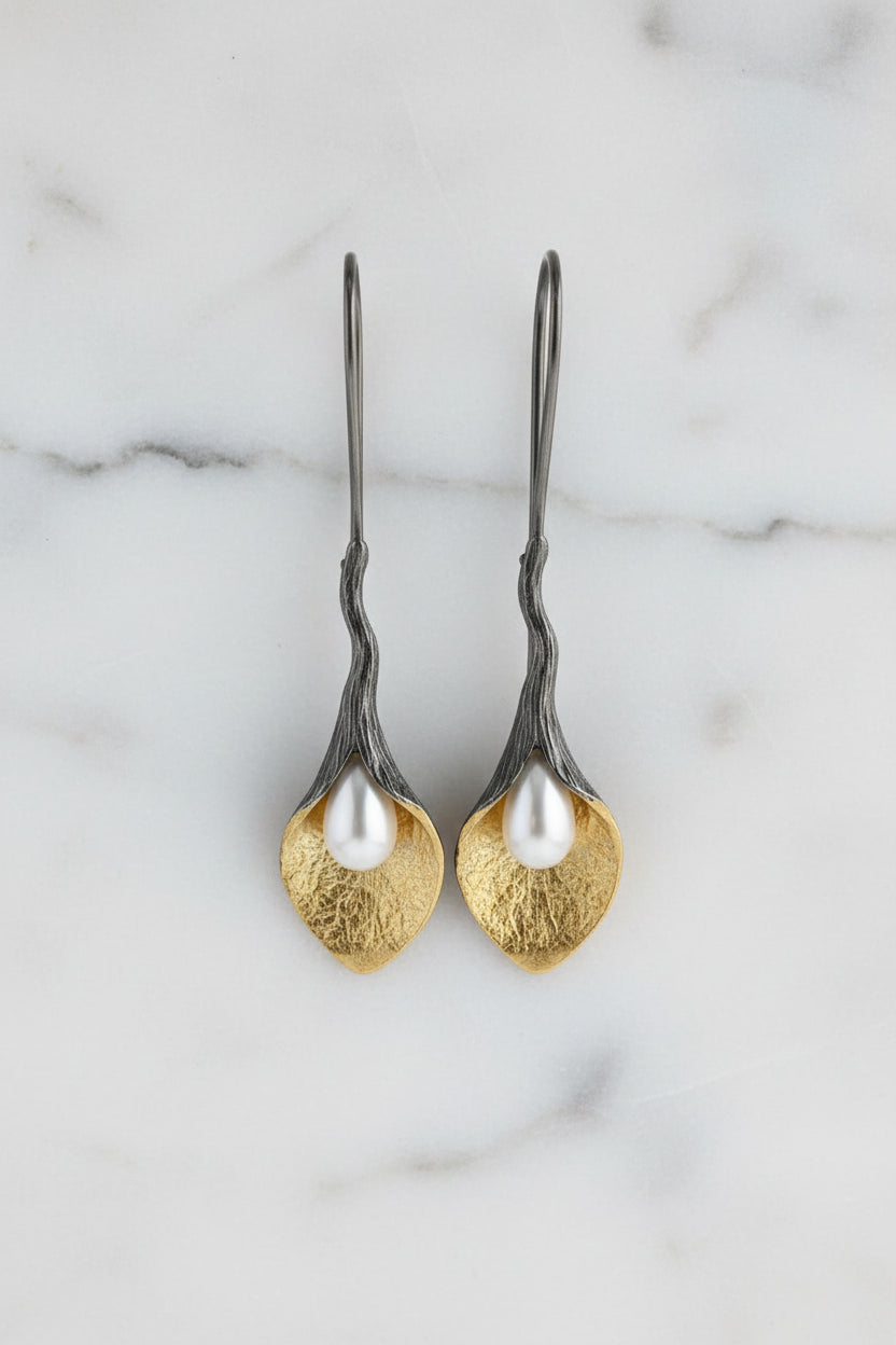 Pair of silver and gold earrings on a beige fabric background