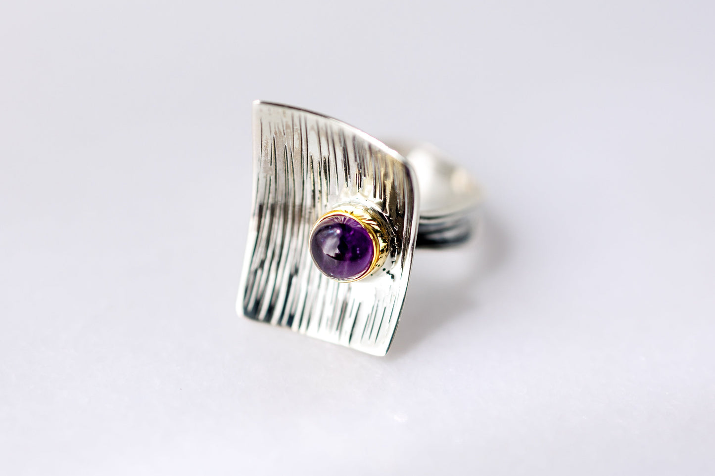Silver ring with a purple gemstone on a light gray background