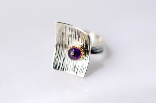 Silver ring with a purple gemstone on a light gray background